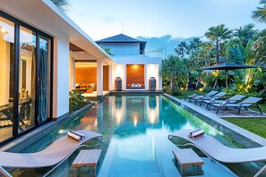 A modern pool area with lounge chairs and a view of a building with a balcony. - Villa Castil di Udara by Villa Finder (Kerobokan)