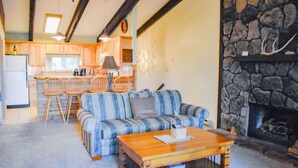 A cozy living room with a striped sofa, wooden coffee table, and a stone fireplace. - The Nestled Inn - Unit C3 (Ruidoso)