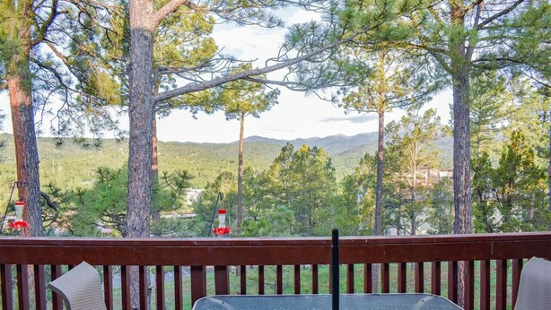 A deck with a table and chairs, overlooking a forested landscape with mountains in the distance. - The Nestled Inn - Unit C3 (Ruidoso)