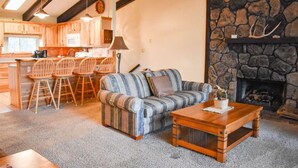 A cozy living room with a striped sofa, wooden coffee table, and stone fireplace. - The Nestled Inn - Unit C3 (Ruidoso)
