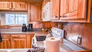 A kitchen with wooden cabinets, a stove, a coffee maker, and a window. - The Nestled Inn - Unit C3 (Ruidoso)