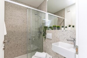 A modern bathroom with a glass-enclosed shower, a white sink, and a mirror above the sink. - Pool Sapore Di Mare Apartments (Baska)