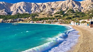 A coastal beach with clear turquoise waters, a pebbly shore, and a backdrop of rocky mountains. - Pool Sapore Di Mare Apartments (Baska)