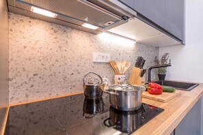 A modern kitchen with a black countertop, stainless steel kettle, pot, and a red bell pepper. - Pool Sapore Di Mare Apartments (Baska)