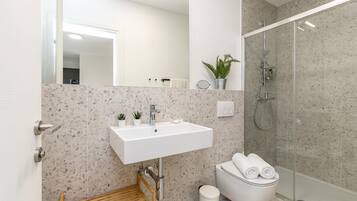 A modern bathroom with a freestanding sink, a toilet, a shower, and a small wooden shelf.