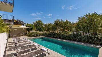 A swimming pool with sun loungers and a clear blue sky.