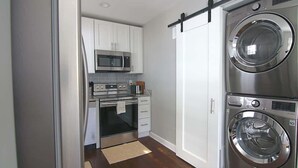 A compact kitchen with white cabinets, a microwave, an oven, and a double stainless steel washer and dryer unit. - Downtown Silver Spring Ranch home! (Silver Spring)