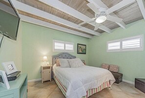 A bedroom with a bed, a nightstand, a desk, a ceiling fan, and a window.