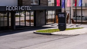 The exterior of the Ador Hotel with a modern facade, multiple flags, and a clear entrance sign. - Ador Hotel (Pristina)