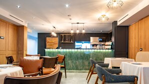 A modern restaurant interior with wooden panel walls, a marble counter, and a mix of leather and fabric chairs. - Ador Hotel (Pristina)