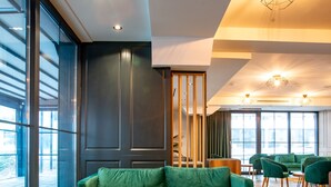 A modern interior with green upholstered seating, a wooden coffee table, and large windows providing natural light. - Ador Hotel (Pristina)