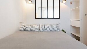 Une pièce minimaliste comprenant un lit, une fenêtre avec des stores et une étagère intégrée.