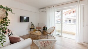 Un salon moderne avec un canapé, une table basse, des fauteuils en osier et un téléviseur.