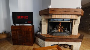 Un salon avec une cheminée, un téléviseur affichant le logo « NETFLIX » et un meuble en bois.