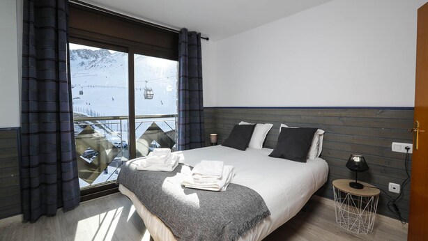 Une chambre avec un grand lit, une vue sur une piste de ski et une fenêtre avec des rideaux.