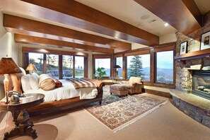 Relax in this elegantly furnished living room with a high ceiling and fireplace, featuring a comfortable sofa and large windows offering a mountain view.