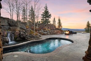 Surrounded by evergreen trees, this pool features a waterfall and fire pit area with seating.