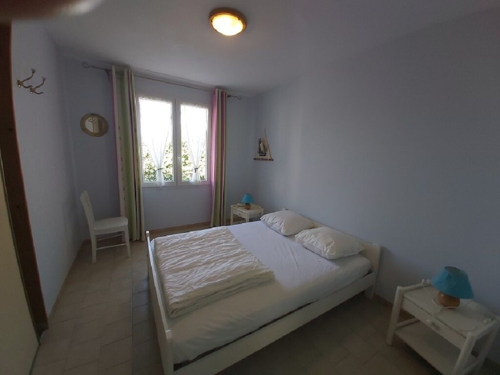 Een slaapkamer met een bed, een stoel, een nachtkastje, een lamp en een raam met gordijnen.
