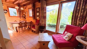 Een gezellig cabin interieur met een eethoek, een rode bank en een groot raam met uitzicht op de bergen.