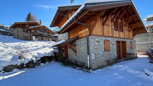 Een houten chalet met stenen muren, een balkon en een skilift op de achtergrond.