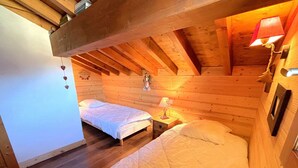 Een gezellig slaapkamer op zolder met twee bedden, houten balken en een schuine kap.