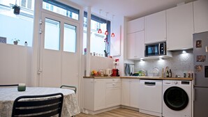 Cocina compacta con lavadora, microondas y comedor con mesa y sillas.