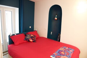 A bed with red bedding, a patterned throw, and a unique door design.