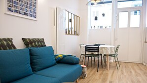 Una sala de estar con un sofá azul, una mesa de comedor con sillas y una mesita redonda con una bandeja.
