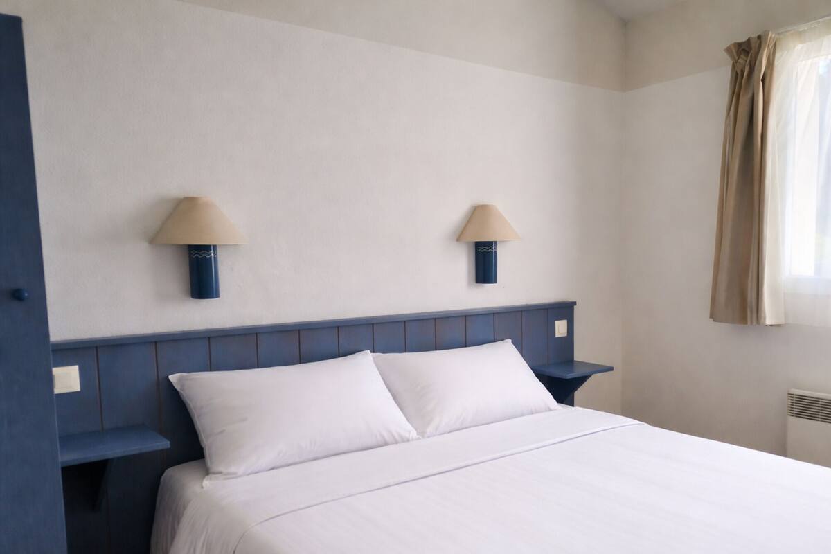 Ein Hotelzimmer mit einem Bett, zwei Wandlampen und einem mit Vorhängen versehenen Fenster.