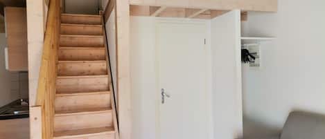 A wooden staircase leading to a white door, a gray sofa, and a small white shelf with a picture.