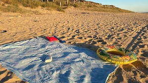 A sandy beach with a blue blanket, a red toy, a blue paddle, and a yellow inflatable ring. - Olydea Oléron les Sables Vigniers (Saint-Georges-d'Oleron)