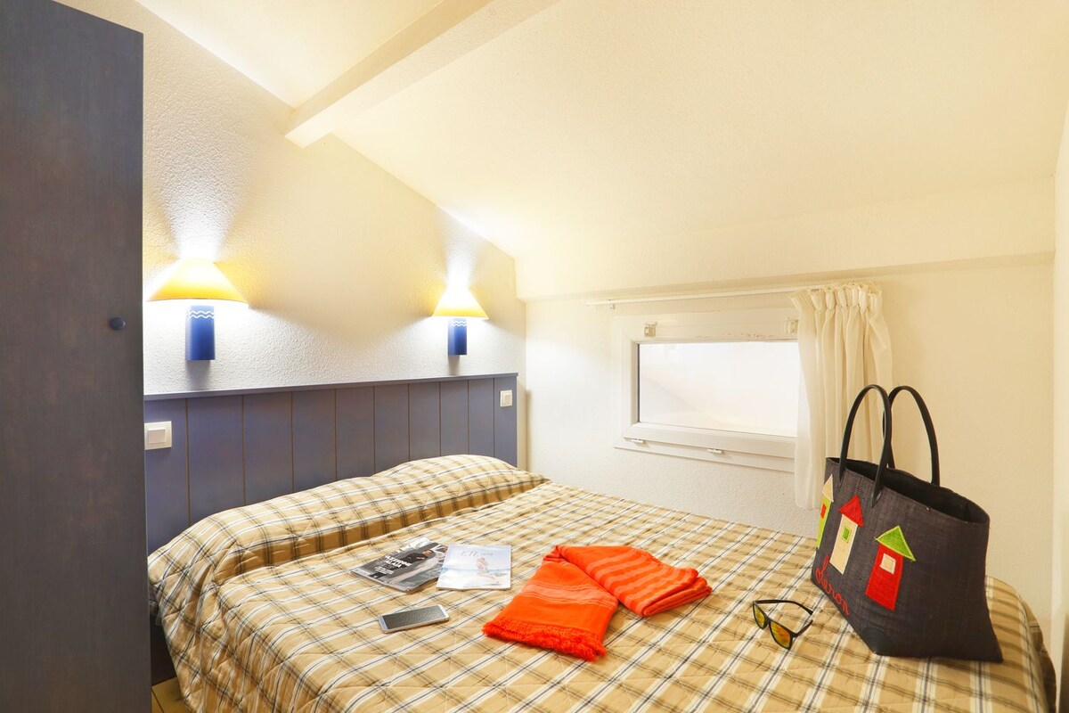 Una habitación de hotel con una cama, dos lámparas de pared, una ventana con cortinas y un bolso sobre la cama.