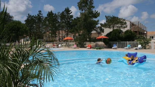 A swimming pool with people and inflatable toys, surrounded by trees and umbrellas. - Olydea Oléron les Sables Vigniers (Saint-Georges-d'Oleron)
