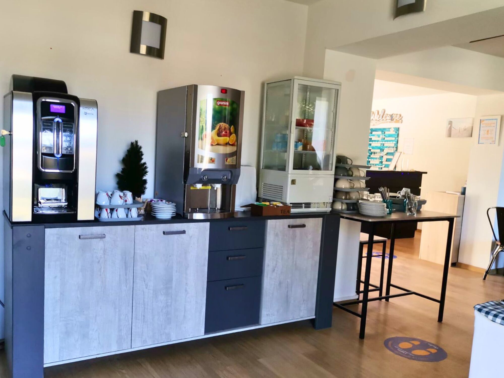 Een moderne keuken met een koffieapparaat, een gekoelde vitrine en een theeset.
