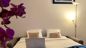 A hotel room with a bed, a laptop, a bedside lamp, a framed picture on the wall, and a table with a glass of water. - Olydea Oléron les Sables Vigniers (Saint-Georges-d'Oleron)