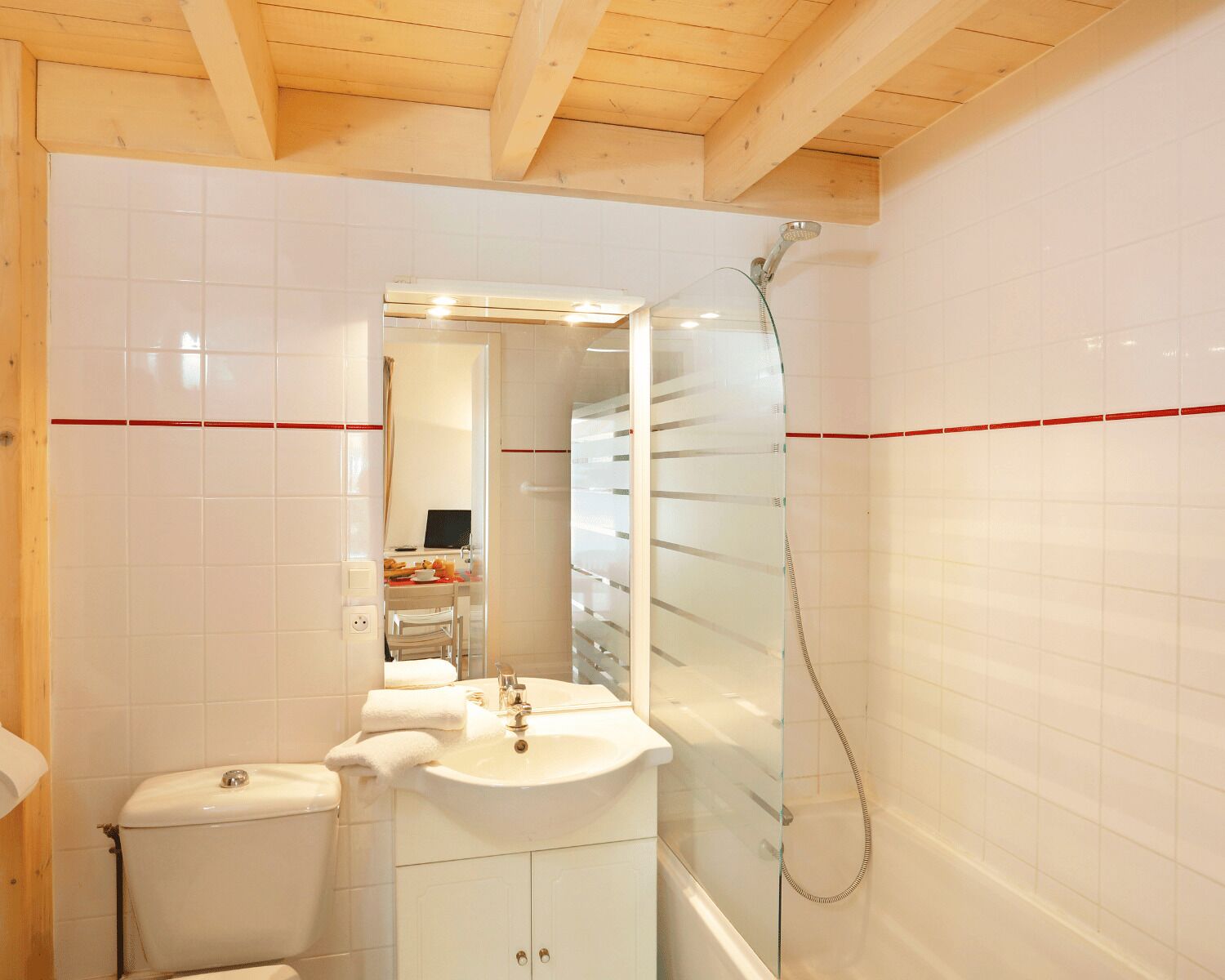 Ein Badezimmer mit weißen Fliesen, Toilette, Waschbecken, Spiegel und Dusche.