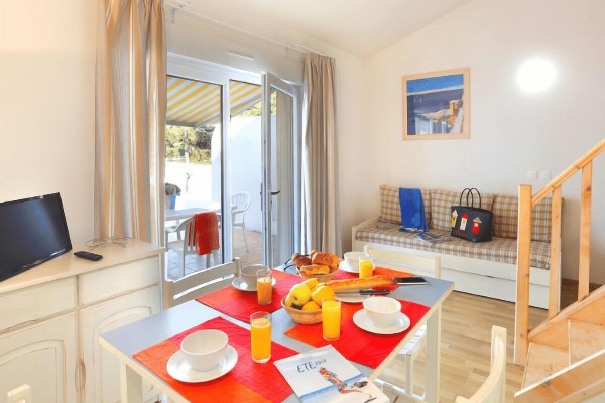 Un comedor con una mesa preparada para el desayuno, un sofá con un bolso y un televisor sobre un mueble.