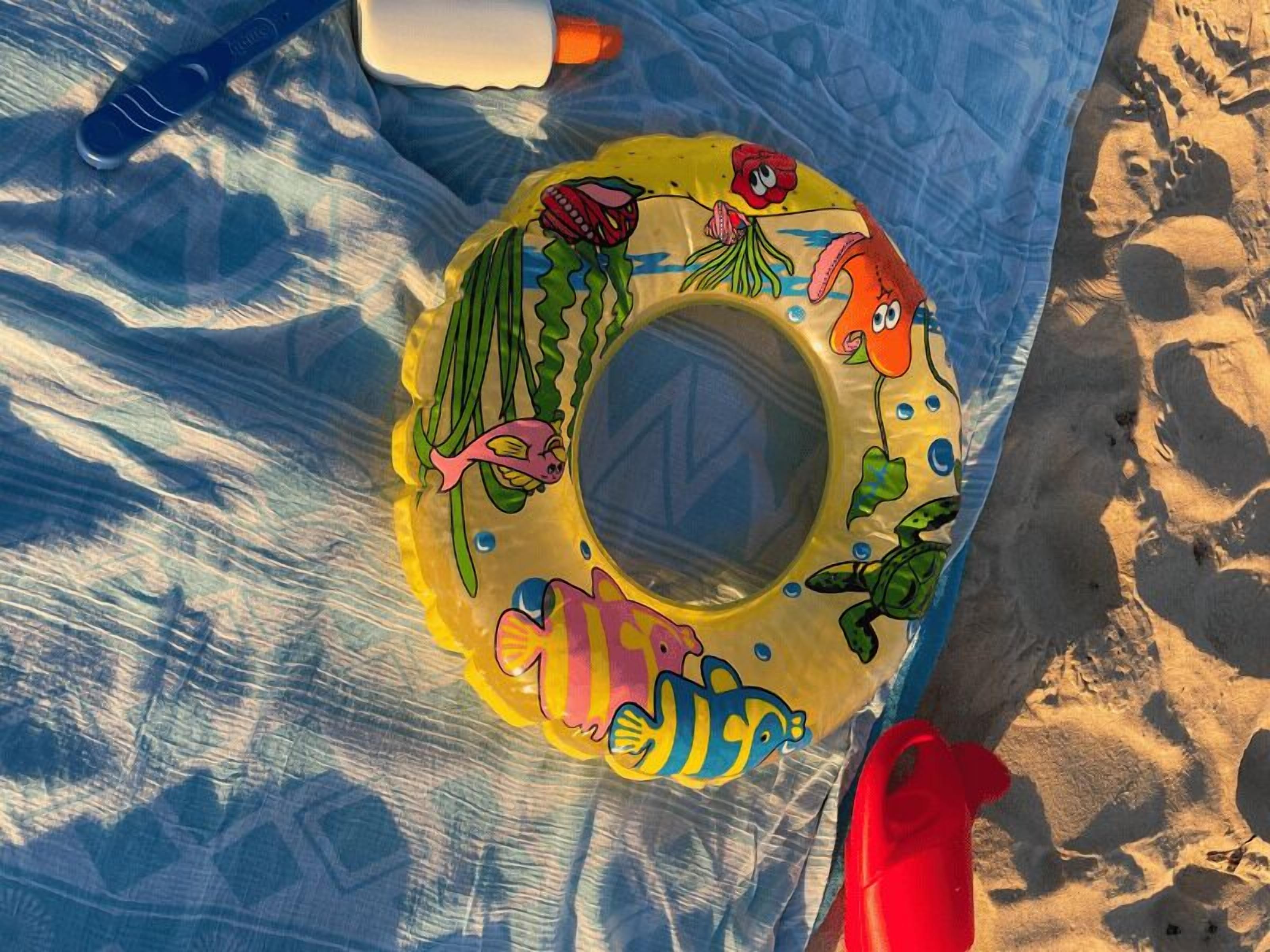 Een strandlaken met een rond opblaasbaar ringetje met tekenfilmzeedieren.