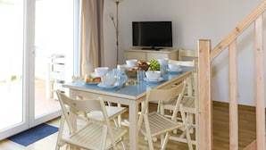 A dining area with a table set for four, a television on a stand, and a staircase to the right. - Olydea Oléron les Sables Vigniers (Saint-Georges-d'Oleron)