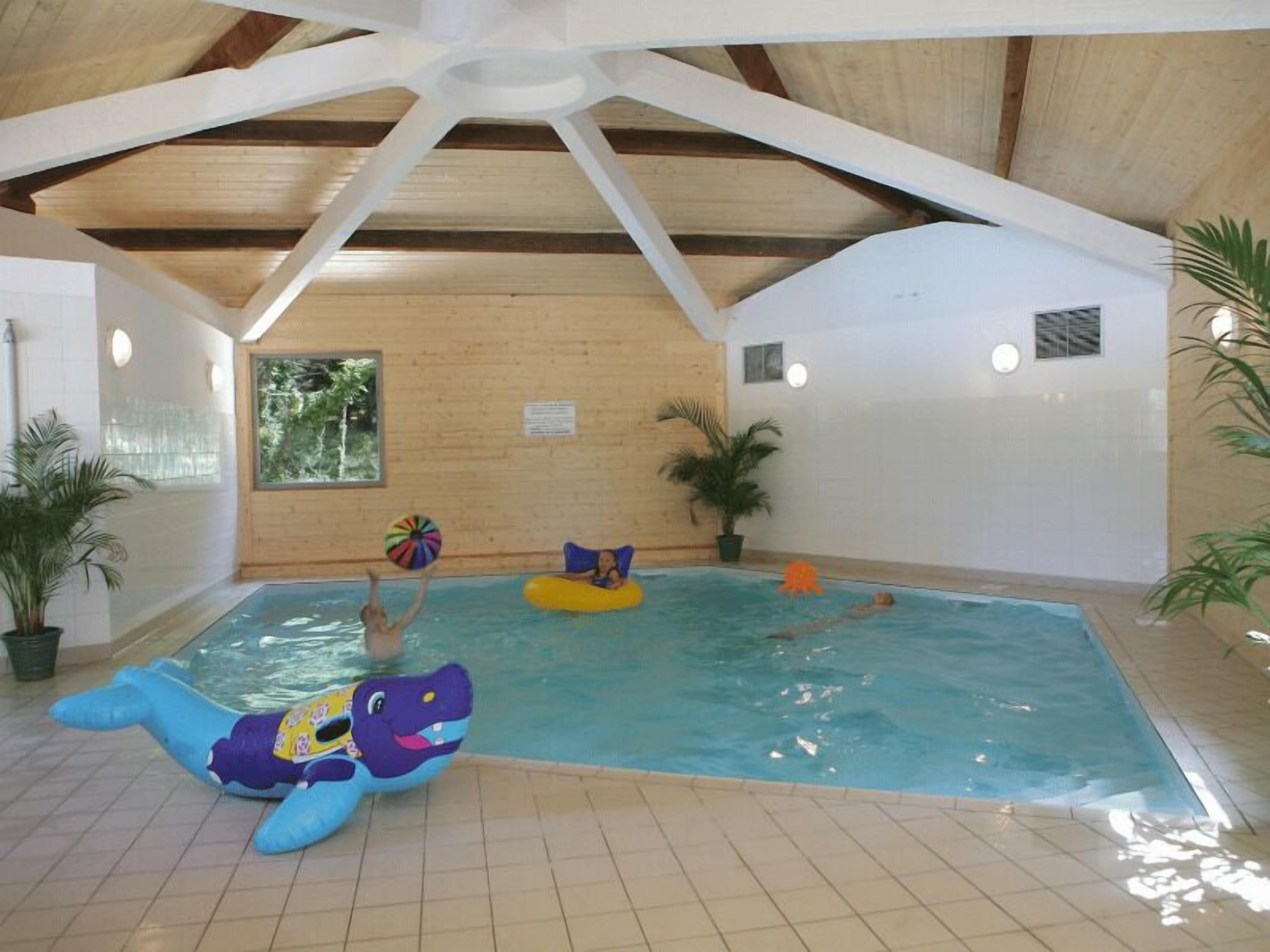 An indoor swimming pool with wooden beams, tiled floor, and inflatable toys.