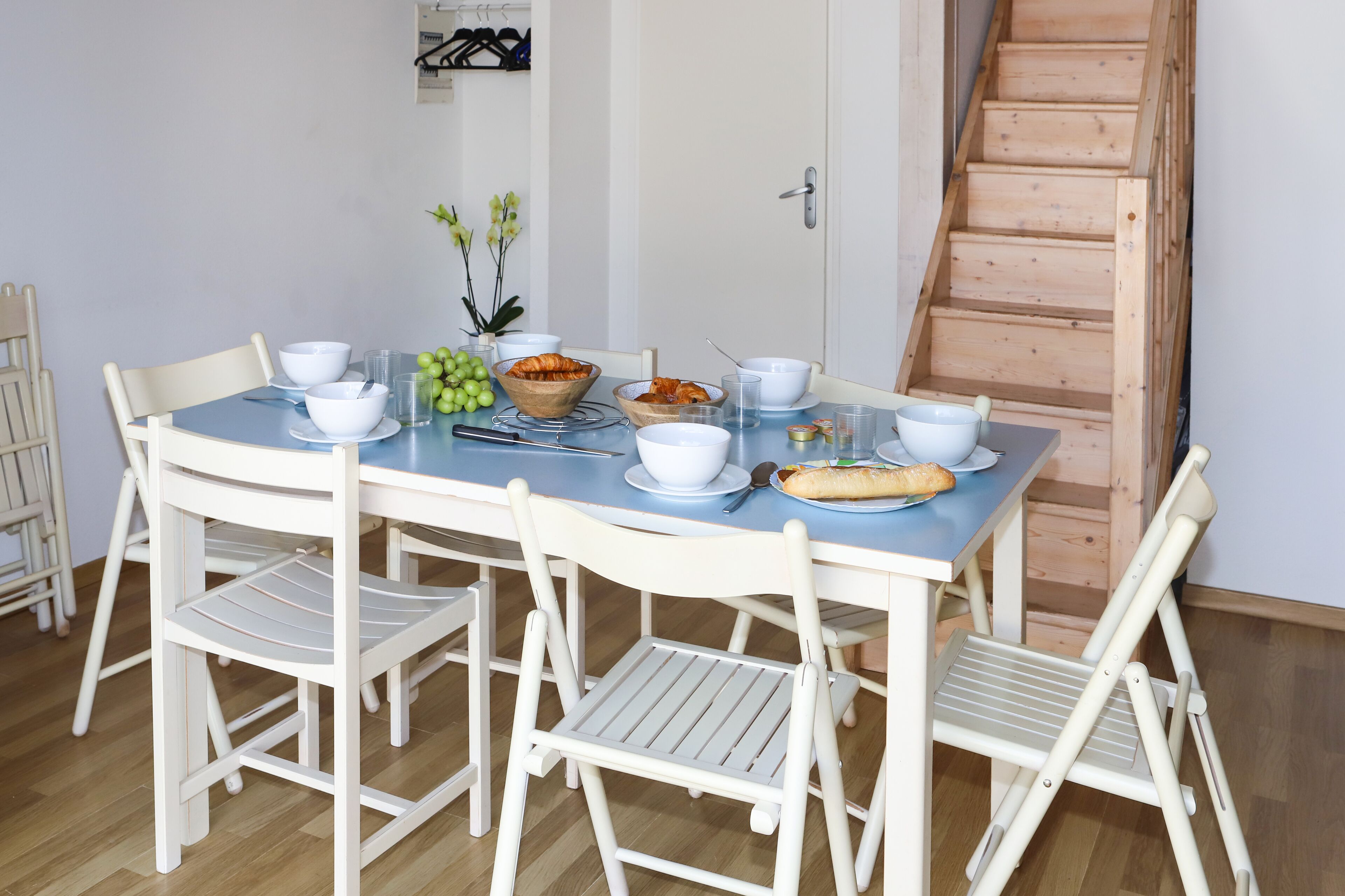 A dining table set with white bowls, plates, and cutlery, surrounded by white chairs.