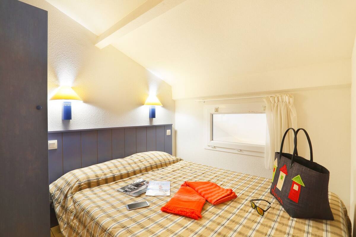 Ein Hotelzimmer mit einem Bett, zwei Wandlampen, einem fensterbelaubten Fenster und einer Tasche auf dem Bett.