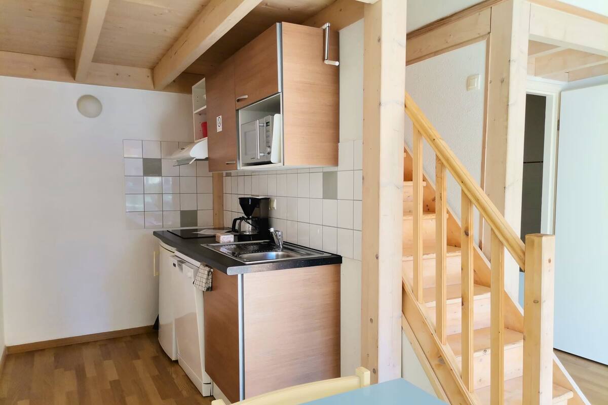 Eine kompakte Küche mit Mikrowelle, Kaffeemaschine und Spüle. Eine Holztreppe führt zu einer weiteren Ebene.
