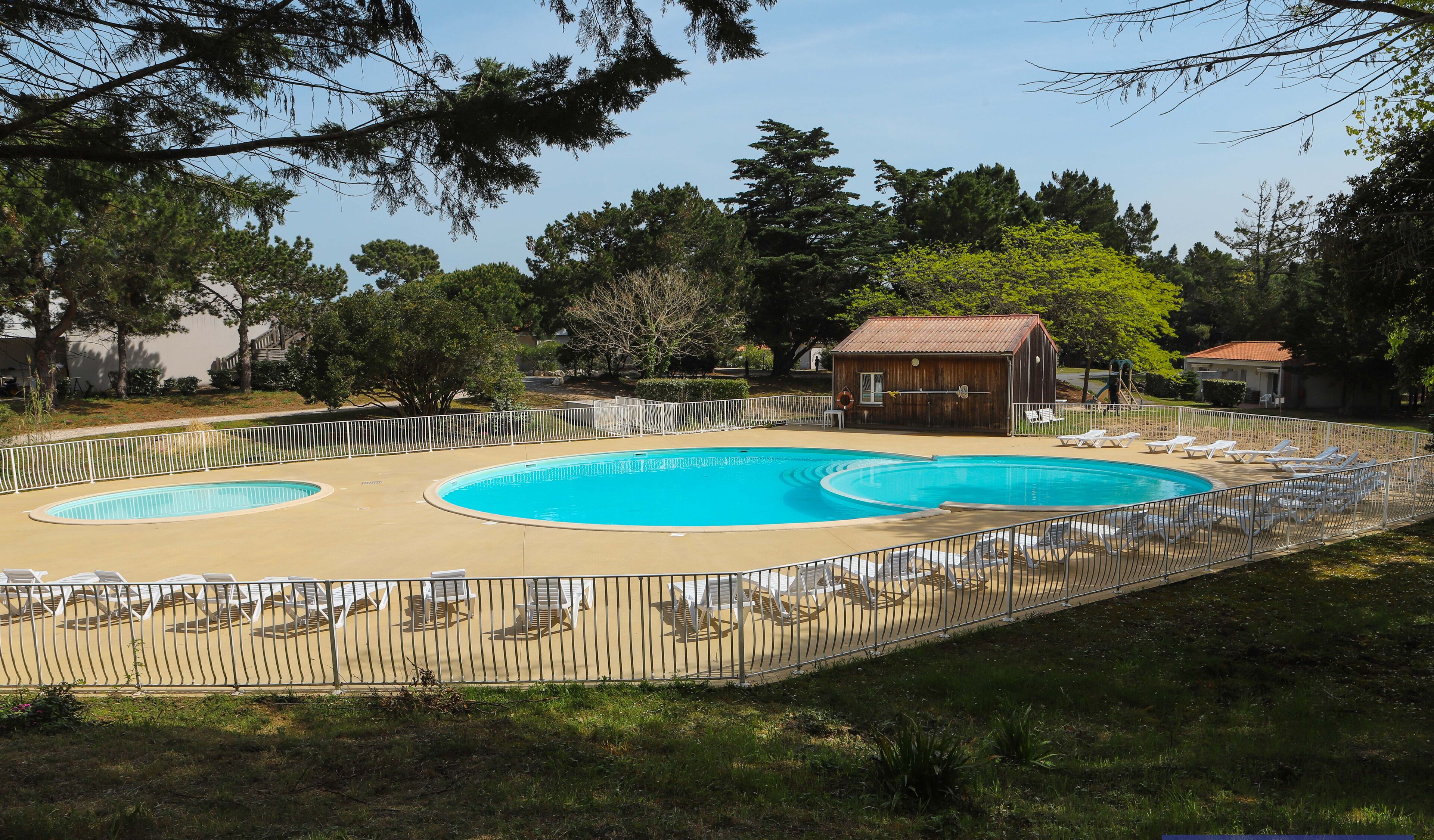 Una piscina con dos secciones, rodeada por una valla y un pequeño edificio al fondo.