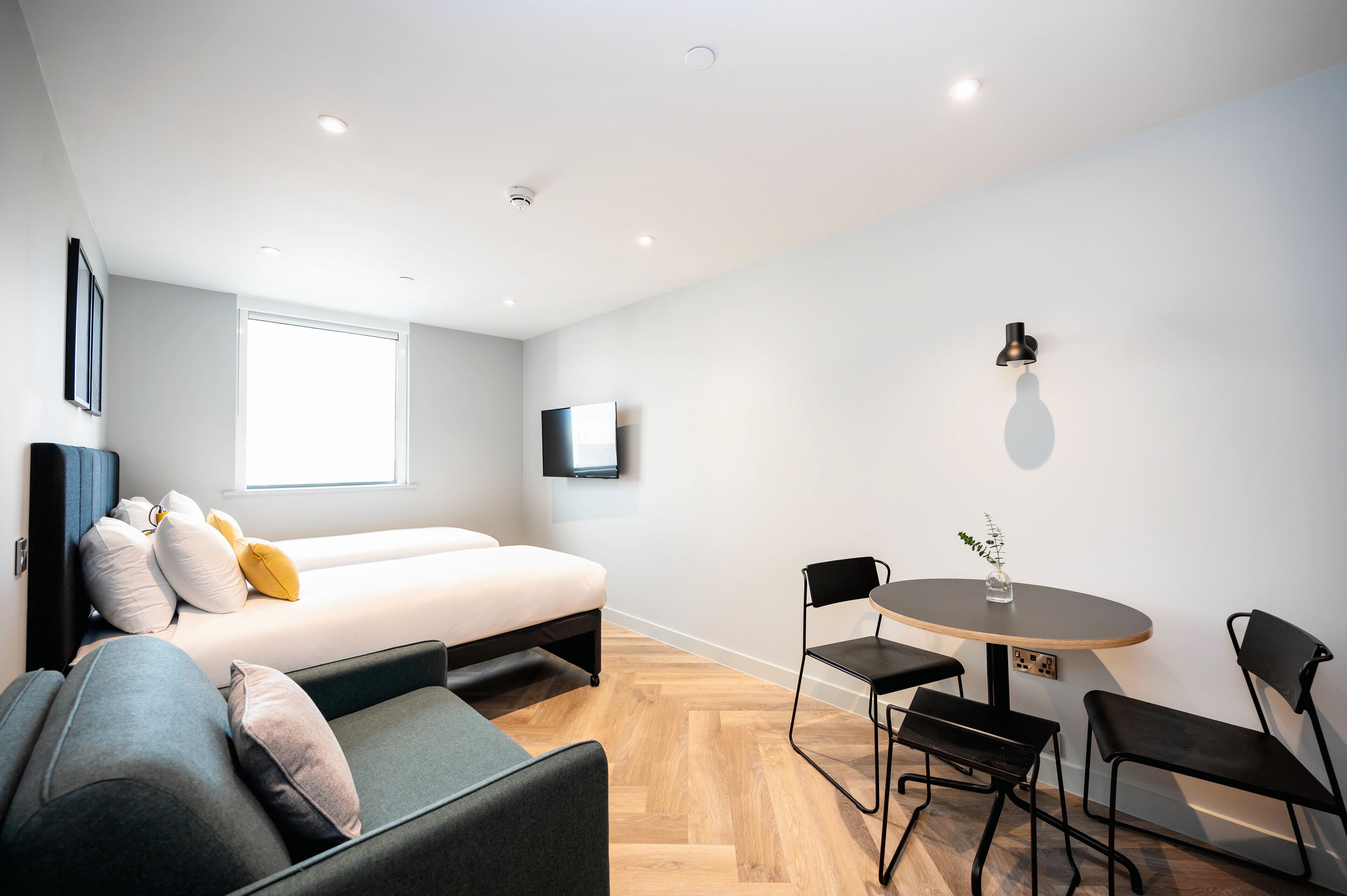 A modern, compact room with a bed, sofa, and a dining area with chairs and a table.