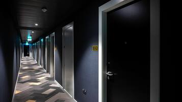 A hotel corridor with a chevron-patterned carpet, dark walls, and doors numbered 001.