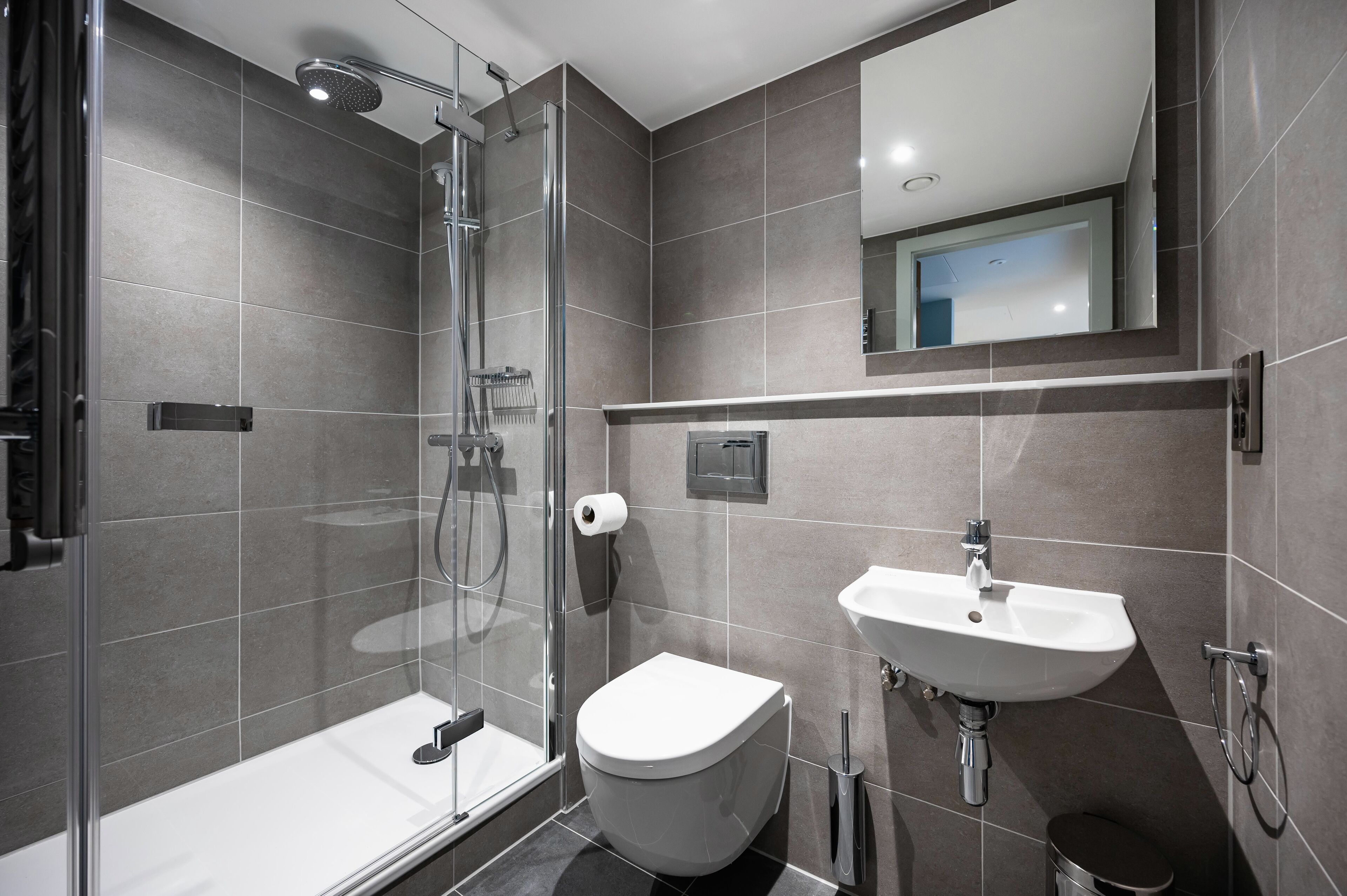 A modern bathroom with a glass-enclosed shower, a white toilet, and a sink with a mirror above it.