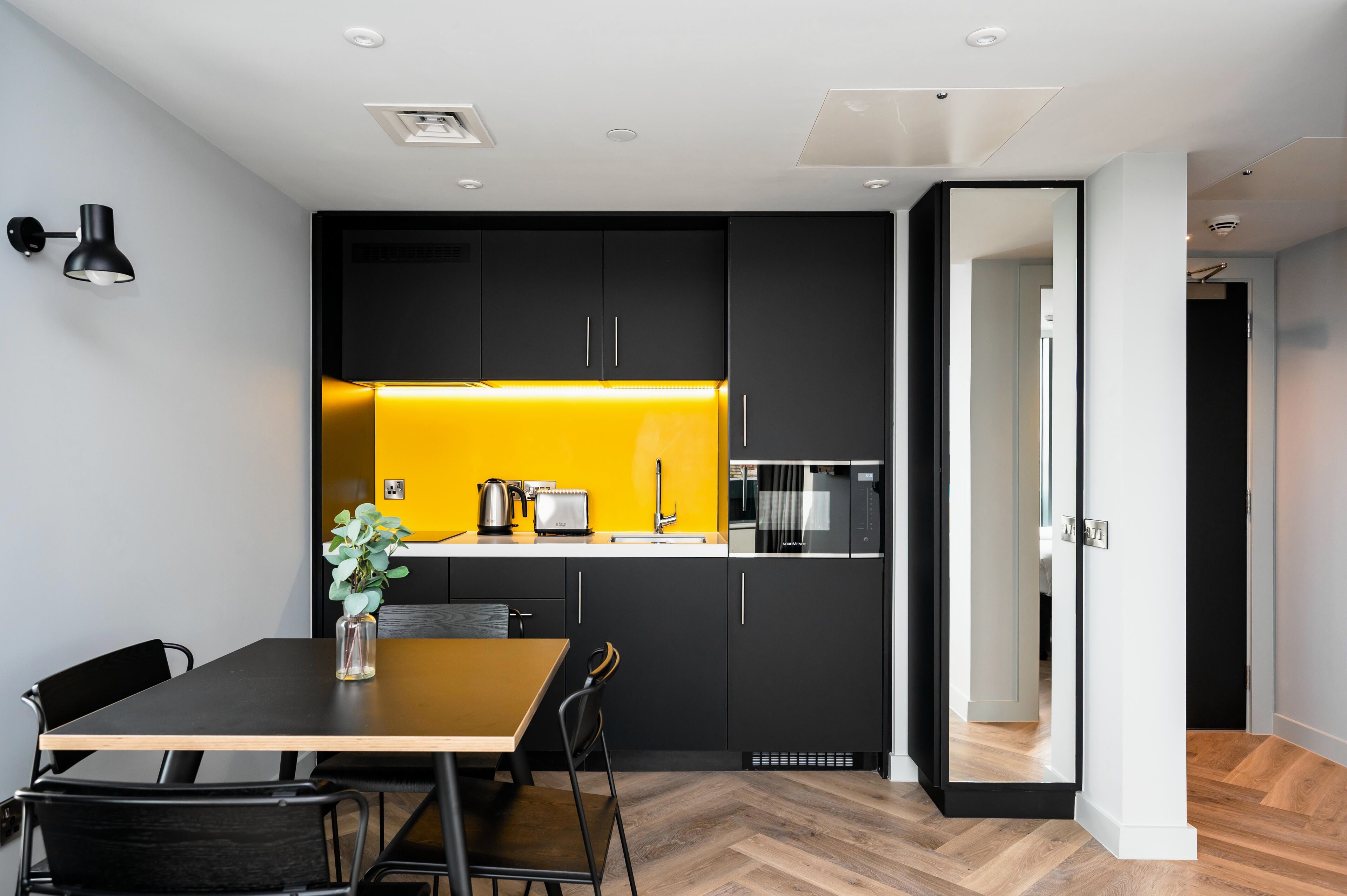 A modern kitchen with black cabinets, a yellow backsplash, and a wooden dining table with chairs.