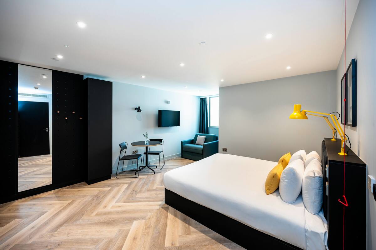 A modern hotel room with a large bed, a desk, a chair, a TV, and a mirror.