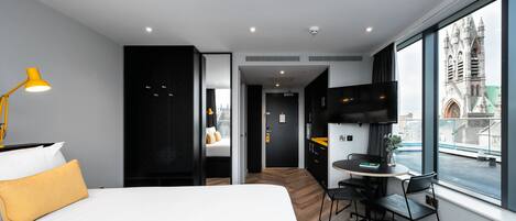 A modern hotel room with a bed, a desk, and a large window offering a city view.